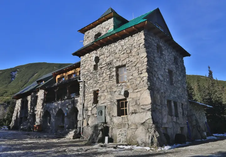 Kamienny budynek schroniska w Tatrach Polskich, z zielonym dachem i widokiem na górzyste tereny.