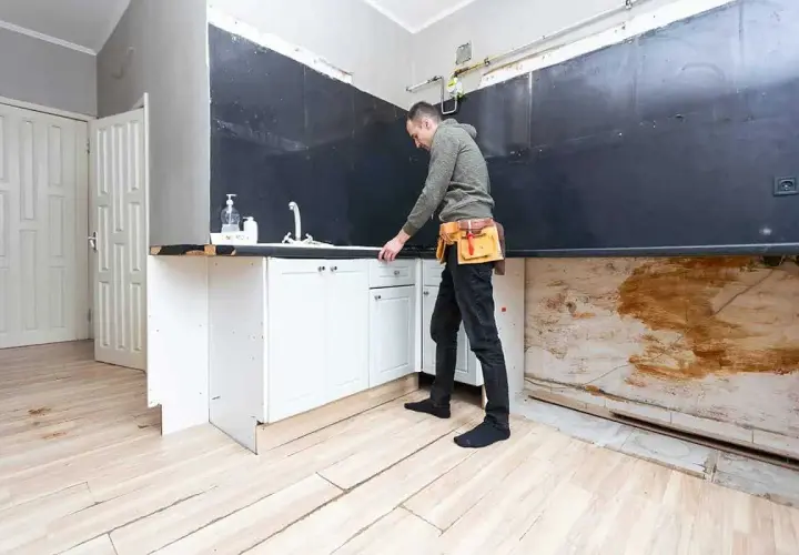 Remont kuchni od czego zacząć? Mężczyzna w pasie narzędziowym sprawdza szafki pod zlewem.