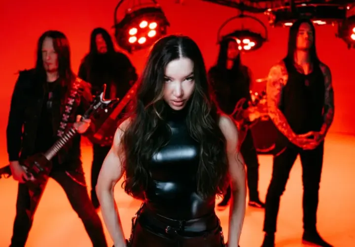 Arch enemy wokalistka w skórzanym stroju, otoczona przez zespół na tle czerwonych świateł.