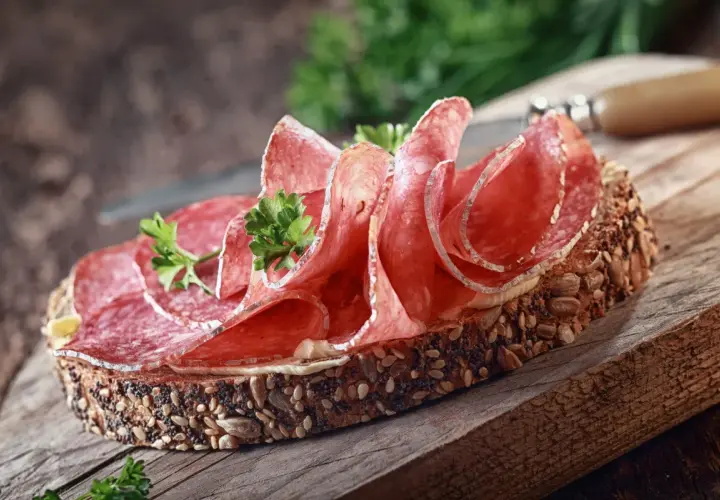 Kanapka z ciemnego pieczywa obficie posypanego ziarnami, z plasterkami aromatycznego salami i natką pietruszki.