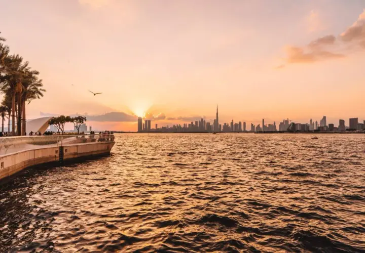 Sonnenuntergang über Dubai. Die Skyline mit dem Burj Khalifa und Palmen am Ufer sind einige der Dubai Highlights.