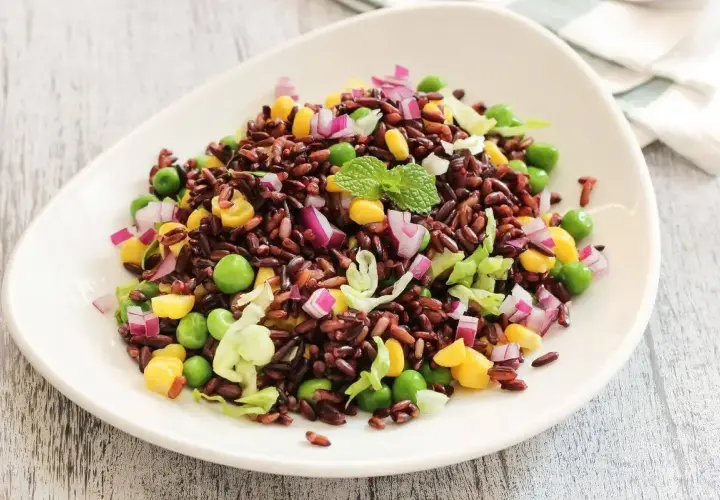 Insalata di riso Venere colorata con piselli, mais, cipolla rossa e lattuga croccante, guarnita con menta fresca.