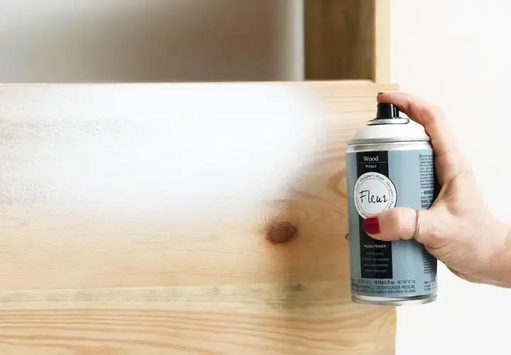 Mano aplica imprimación en spray a madera. Es necesario imprimar antes de pintar madera para un acabado perfecto.