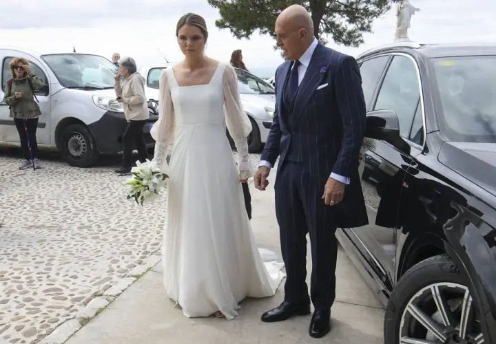 Novia con ramo de lirios y su acompañante, un hombre con traje de raya diplomática, llegan a su boda. Irene Matamoros, radiante.