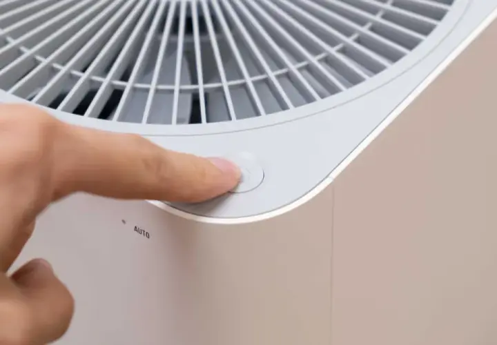 Dedo presionando el botón de encendido de un purificador de aire con filtro de ozono.
