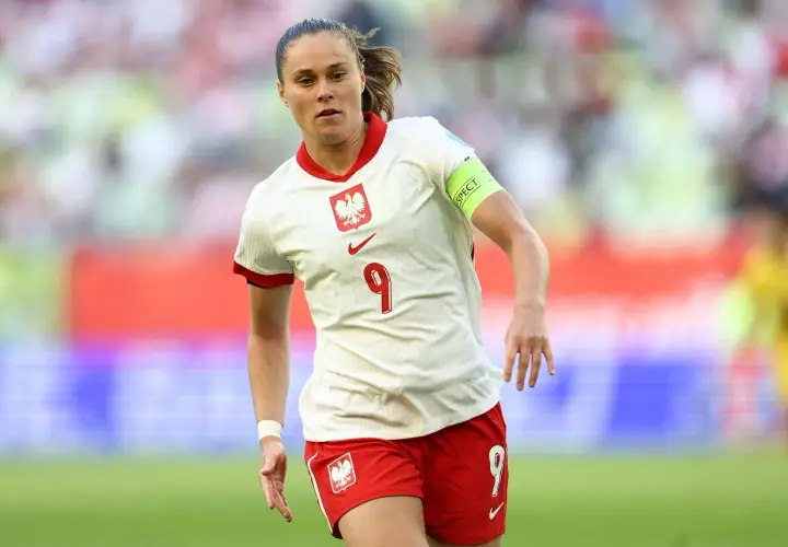 Piłkarka w białej koszulce z orłem i numerem 9, w czerwonych spodenkach. Reprezentuje polska dania na boisku.