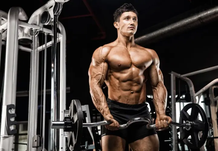 Mężczyzna z wyrzeźbionym ciałem wykonuje ćwiczenia na biceps z łamaną sztangą w siłowni.
