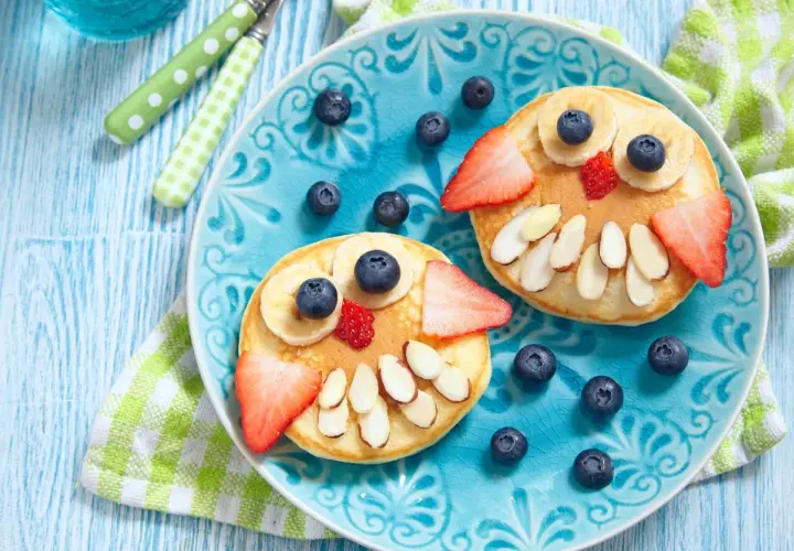 Due pancake a forma di gufo, decorati con frutta e mandorle, per una colazione sana bambini.
