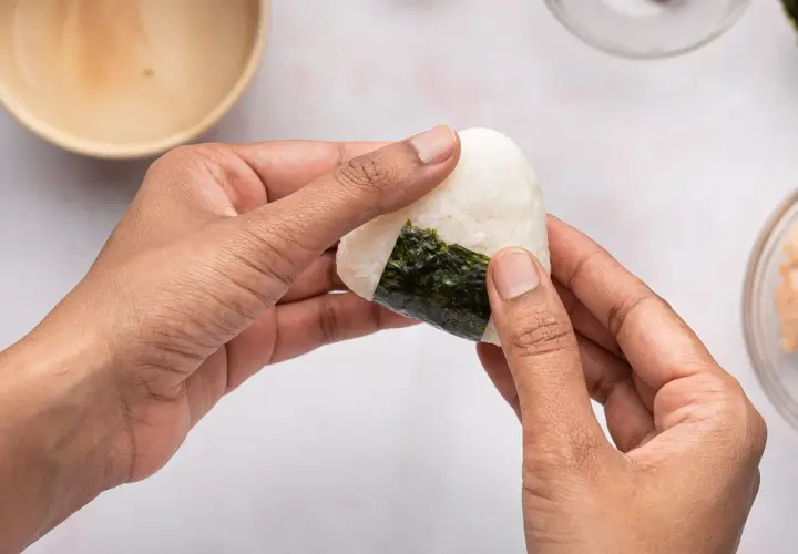Hands shaping a perfectly sized onigiri, a delicious rice ball wrapped in nori seaweed.