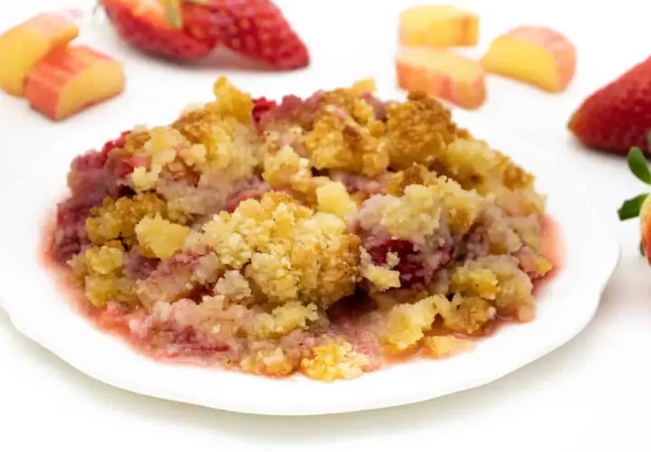 Ein Teller mit warmem Erdbeer-Crumble, garniert mit frischen Erdbeeren und Apfelstücken.