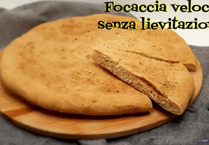 Focaccia veloce senza lievitazione su tagliere di legno. Una fetta è stata tagliata per mostrare la morbidezza.