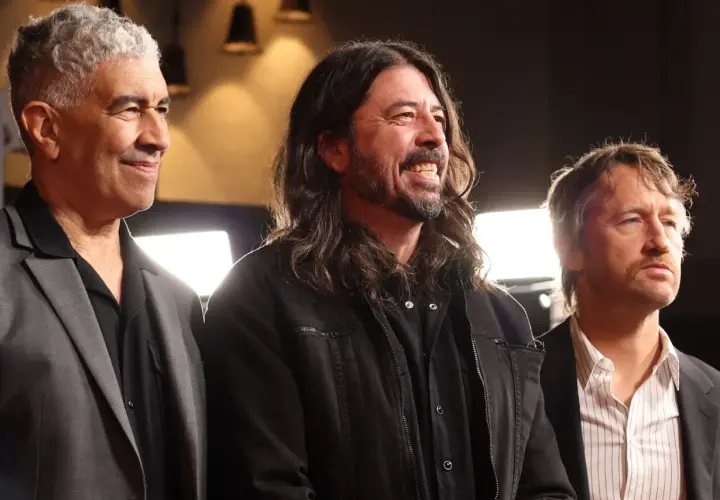 Trzech członków Foo Fighters: Nate Mendel, Dave Grohl i Chris Shiflett, uśmiechają się i patrzą w bok.