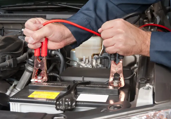 Podłączanie kabli rozruchowych do akumulatora 24v. Mechanik w ciemnej koszuli podłącza czerwone kable do biegunów akumulatora samochodowego.