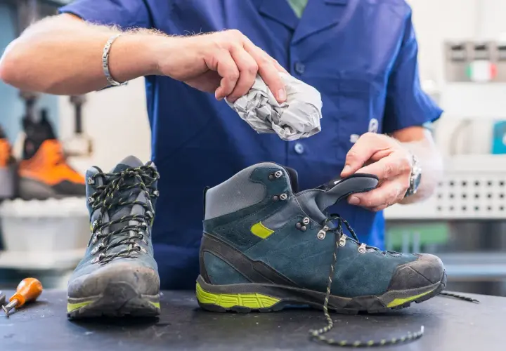 A person stuffs crumpled paper into a hiking boot, demonstrating the best way to dry boots after a muddy adventure.