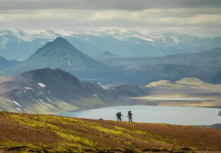 Two hikers on a self-guided Laugavegur trail adventure, with a serene lake and dramatic mountains in the background.