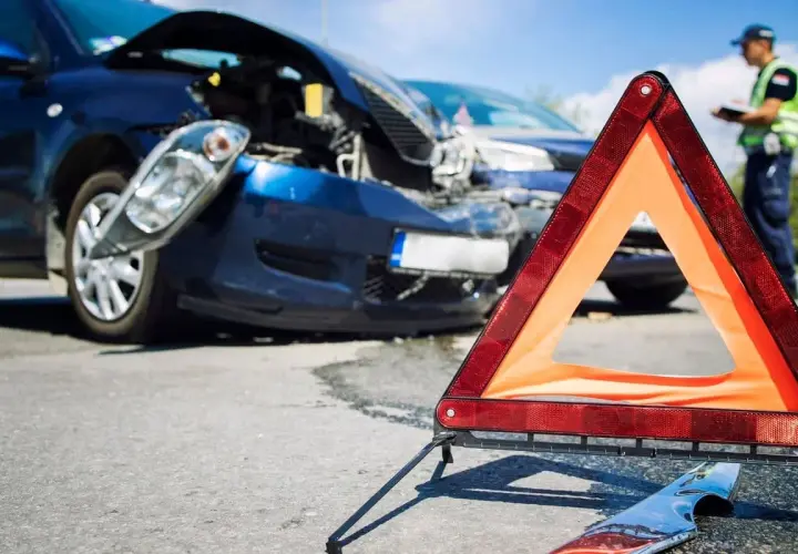 Triangolo di emergenza davanti a due auto danneggiate dopo un incidente. Un poliziotto documenta i danni, forse un incidente senza assicurazione.
