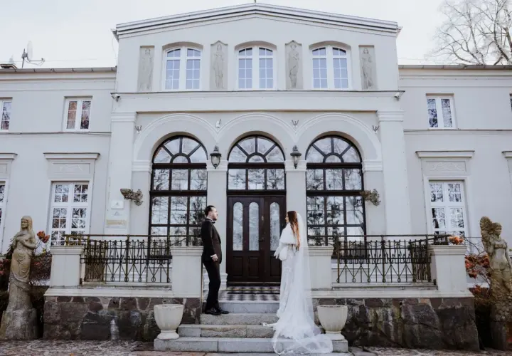 Para młoda przed Lisewskim Dworem. Elegancka biel sukni ślubnej i czarny garnitur pana młodego kontrastują z fasadą zabytkowego budynku.