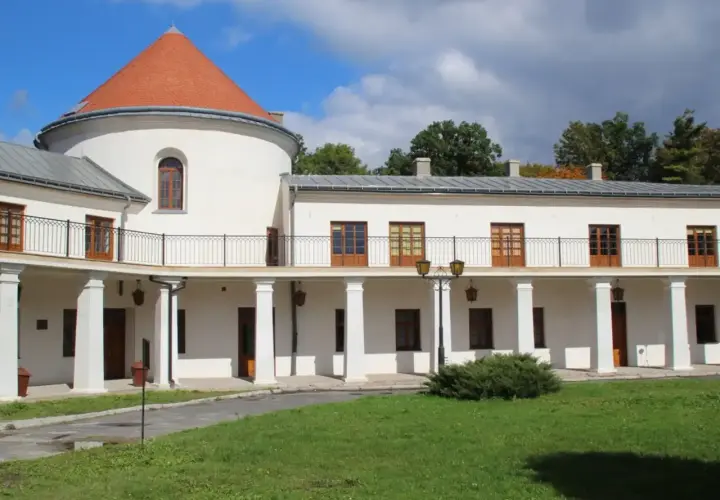Zamek w Lesku, biały budynek z okrągłą wieżą i pomarańczowym dachem, otoczony zielenią.