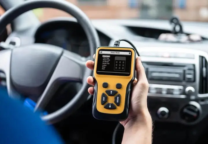 Ręka trzyma żółty skaner diagnostyczny OBD2 w samochodzie, gotowy do porównania z OBD1.