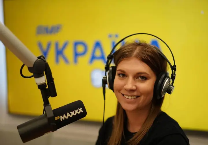 Uśmiechnięta prezenterka w słuchawkach przed mikrofonem. Na tle logo RMF MAXXX, które można usłyszeć na tej samej częstotliwości.