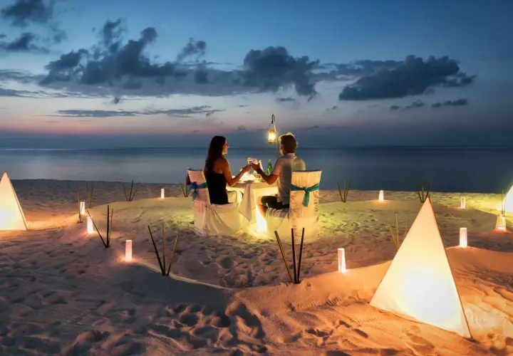 Romantyczna kolacja na plaży. Para świętuje 4 rocznicę ślubu przy blasku lampionów i zachodzącego słońca.