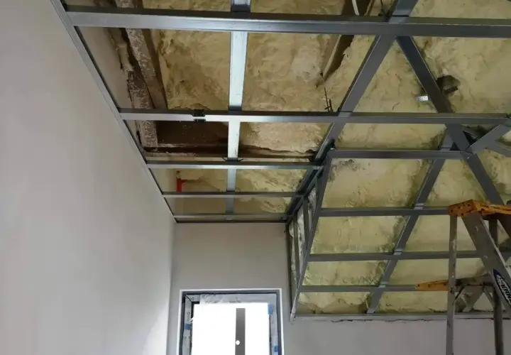 Metalowa konstrukcja pod **sufit** z pianką izolacyjną widać fragment ściany i okna.