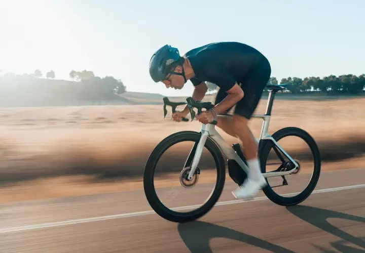 Kolarz w aerodynamicznej pozycji minimalizuje opory toczenia opon rowerowych, pędząc przez krajobraz.