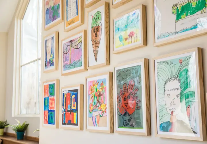 A vibrant kids art gallery wall showcases colorful drawings of ice cream, flowers, and portraits, all framed in light wood.
