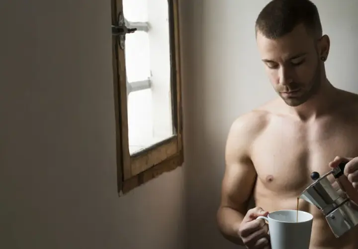 Uomo nudo versa caffè, riflessione sulla psicologia di un uomo sposato. Luce soffusa da una finestra.