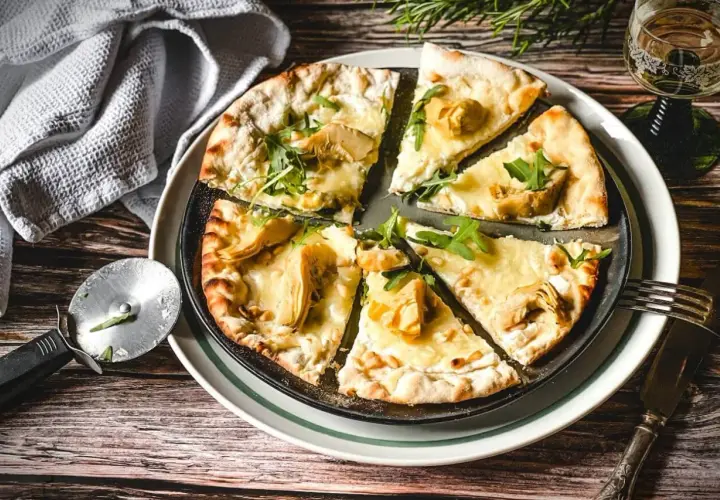 Eine köstliche Pizza Bianca mit Artischocken, Rucola und Pinienkernen, bereit zum Genießen.