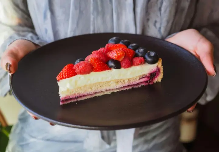 Tranche de tarte aux fruits rouges sur une crème mousseline onctueuse, présentée sur une assiette noire.