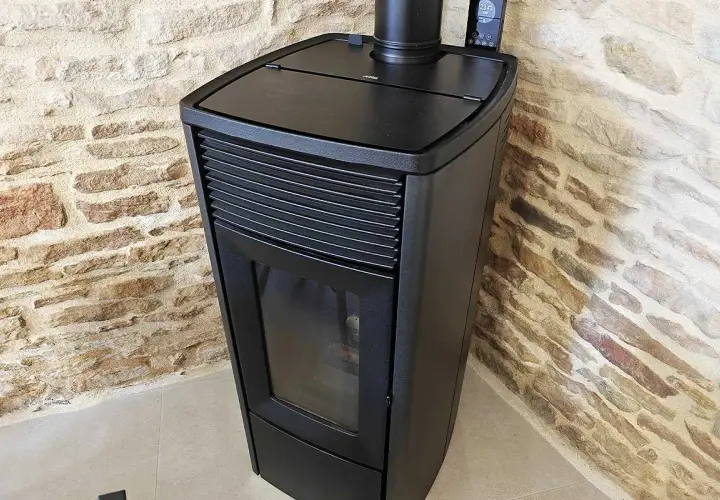 Poêle à granulés noir moderne, avec écran de contrôle, adossé à un mur de pierres. Apprenez comment éteindre un poêle à granulé en toute sécurité.