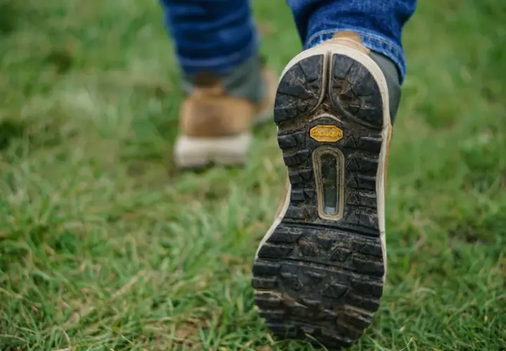 Osoba w dżinsach i butach trekkingowych stawia kroki na trawie. Czy buty trekkingowe powinny być większe? Zobacz podeszwę Vibram.