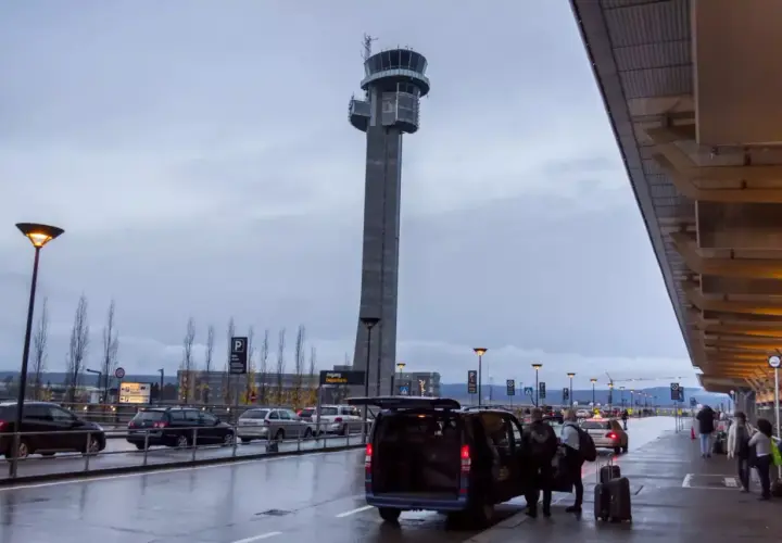 Wieża kontrolna na oslo lotnisko góruje nad mokrym asfaltem i samochodami. Ludzie z bagażami wsiadają do vana.