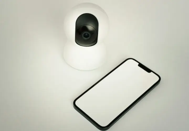 Cámara de seguridad blanca junto a un móvil con pantalla en blanco. Ideal para usar móvil viejo como cámara de seguridad.