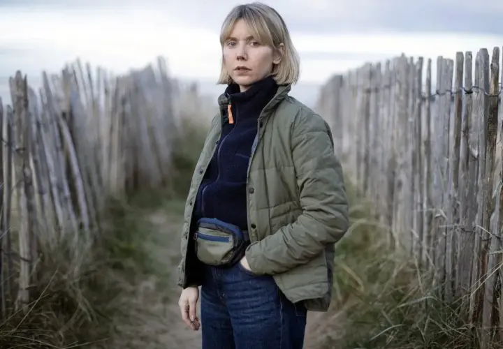 Karen Pirie står vid en vindpinad strand, klädd i en grön jacka och jeans. Hon bär en midjeväska, redo för ett nytt fall.