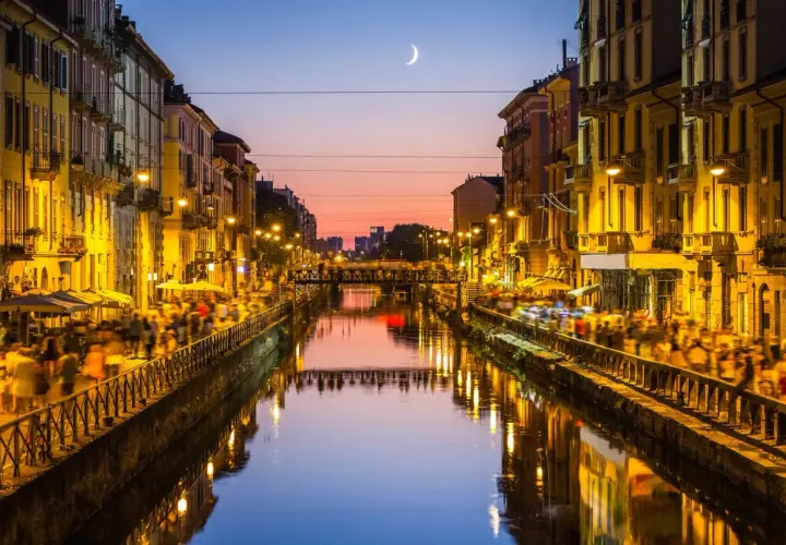 Atardecer en los Navigli de Milán, con gente paseando y luces reflejándose en el canal.