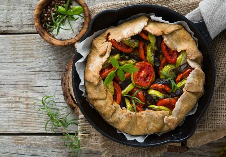 Une rustique quiche aux légumes, garnie de tomates, courgettes et aubergines, prête à être dégustée.