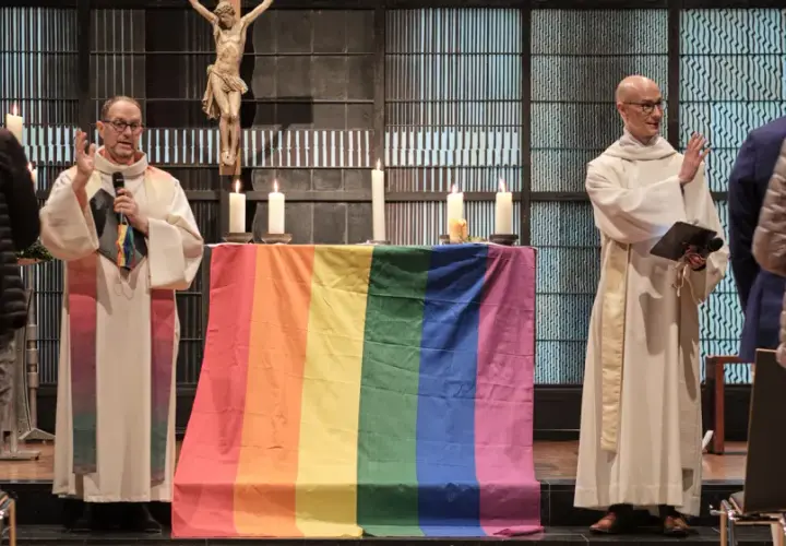 Zwei Geistliche mit Regenbogenfahne und Kreuz im Hintergrund. Ein Gottesdienst für die gleichgeschlechtliche Ehe in der Kirche.
