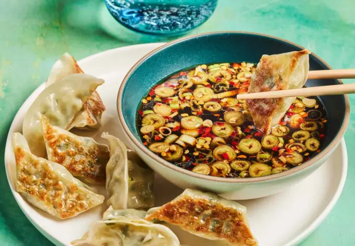 A gyoza is dipped into a flavorful gyoza dipping sauce with scallions and chili flakes.