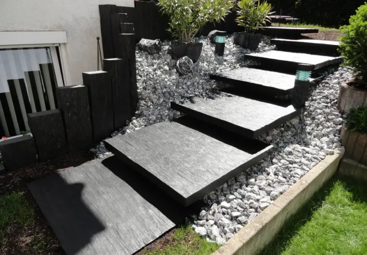 Moderner gartenweg am hang ohne stufen, mit dunklen Steinplatten und Kiesbett.