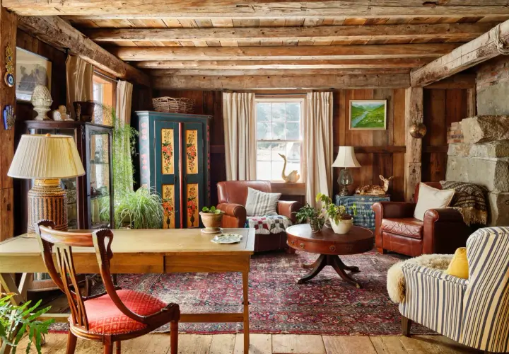 Rustic living room with wooden beams, leather armchairs, a patterned rug, and a vintage cabinet.