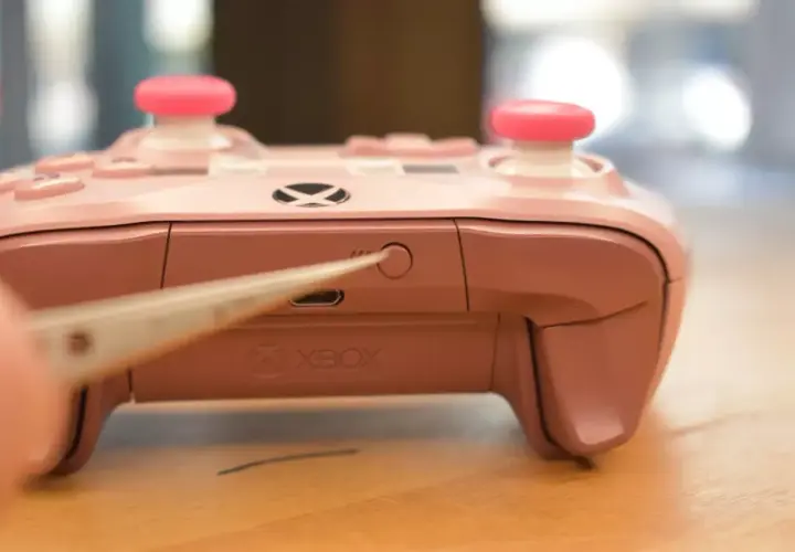Chwytak naciska przycisk parowania na różowym padzie Xbox, pokazując, jak sparować pada Xbox.