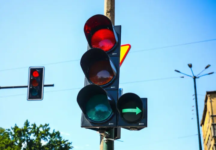 Sygnalizator S2 z zieloną strzałką w prawo i czerwonym światłem na głównym słupku. Niebo błękitne.