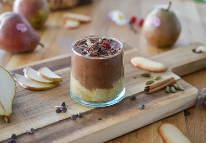 Délicieuse recette mousse poire chocolat, garnie de copeaux de chocolat et d'une framboise. Poires fraîches et épices sur fond de bois.