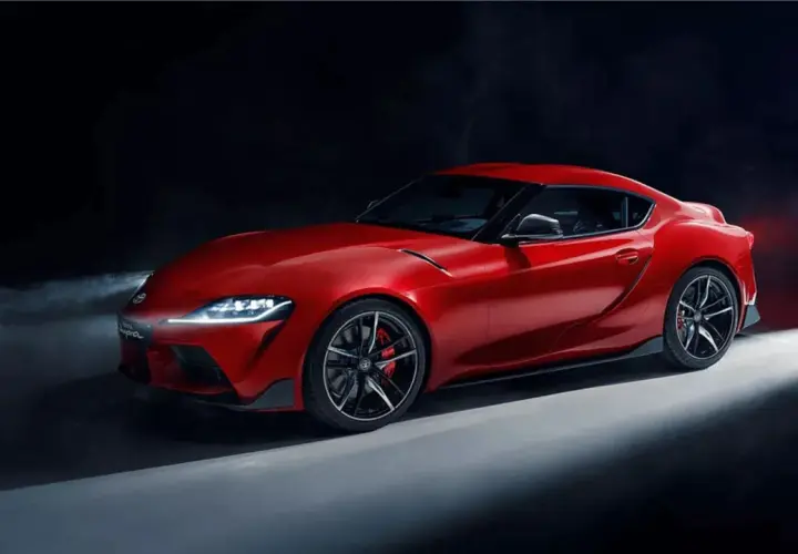 Un deportivo Toyota Supra rojo brillante, con luces encendidas y humo detrás, listo para la acción.