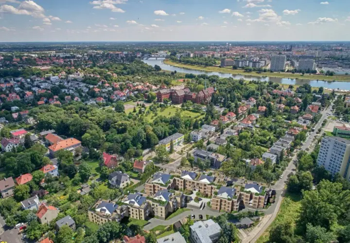 Nowoczesne osiedle w otoczeniu zieleni, z widokiem na rzekę i miasto. W oddali widać zabytkowe budynki i nowe apartamentowce. To idealne miejsce dla osób ceniących spokój i bliskość natury, a jednocześnie dostęp do miejskich atrakcji.