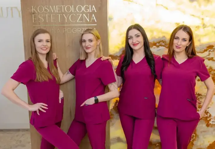 Cztery kobiety w uniformach medycznych stoją obok siebie przed tablicą z napisem "Kosmetologia Estetyczna".