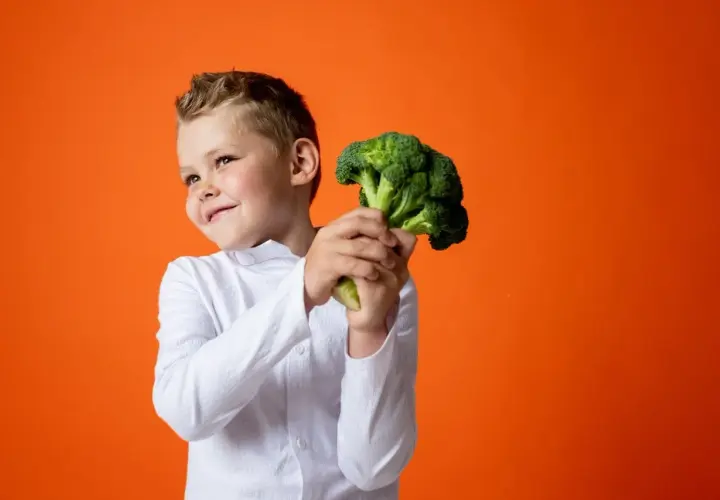 Bambino sorridente con un broccolo, un ortaggio salutare. Non è un legume, ma è ottimo per la salute!