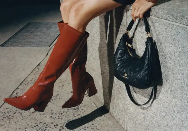 Kobieta w czerwonych kozakach i czarnej torebce z logo Nine West. Nine West to znana marka obuwia i akcesoriów.